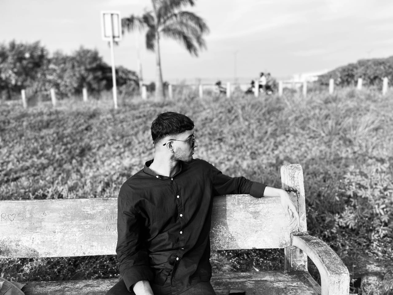 Digital Marketing Expert in Kochi - sitting on a wooden bench outdoors in a grassy area, with a serene background that includes trees and a palm tree.